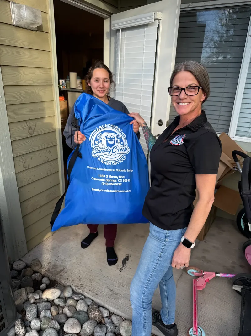 Sandy Creek Laundromat employee delivering a blue laundry bag to a Colorado Springs customer