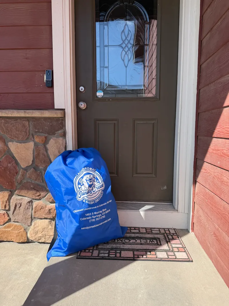 Branded Sandy Creek Laundromat pickup and delivery bag waiting at a Colorado Springs doorstep