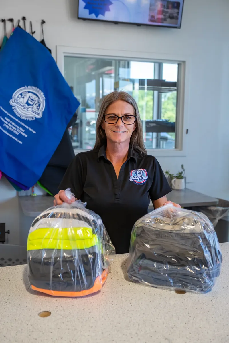 Sandy Creek Laundromat employee presenting freshly folded and packaged laundry orders
