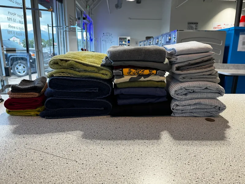 Stacks of professionally folded towels shirts and linens at Sandy Creek Laundromat